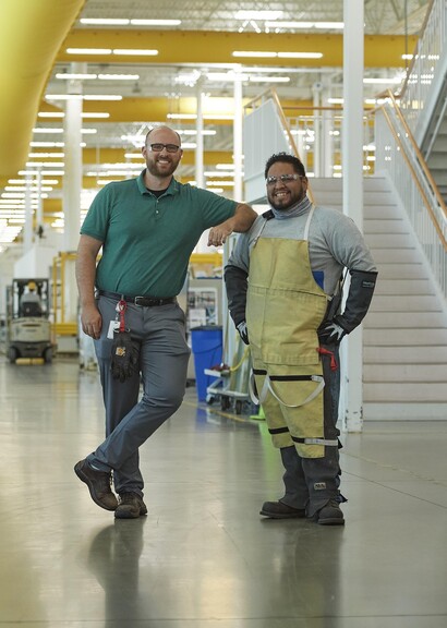 Two coworkers in manufacturing building smiling.