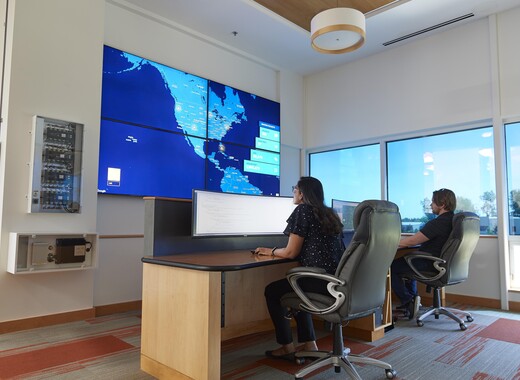 Two woman sitting at a desk working at a computer with a map in the background. 