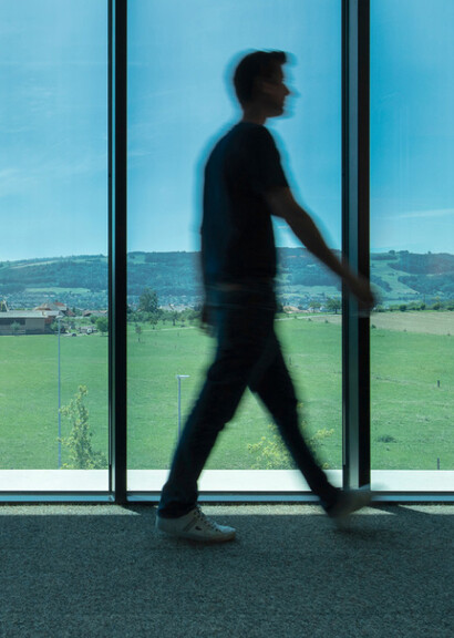 Man walking in front of floor to ceiling smart glass windows overlooking the mountains.