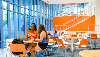 Students collaborate in atrium filled with tables and chairs