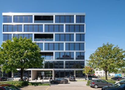 Facade of Alpha Building equipped with SageGlass Bright Silver. Some trees and cars in front of the building.