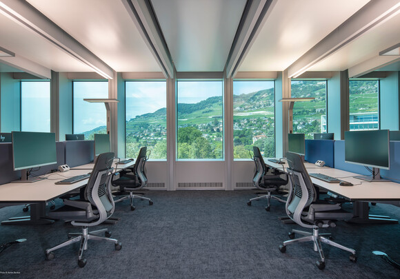 Collaborative office space with smart glass windows from left to right overlooking a mountain side. 