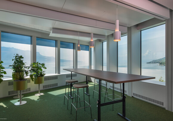 Interior of meeting room with high top table and smart glass windows overlooking the water and mountains. 