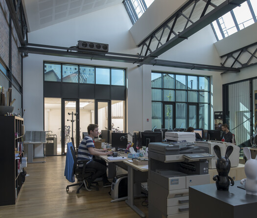 View from the inside of the building. People are working on computers, some windows are tinted, others don't.