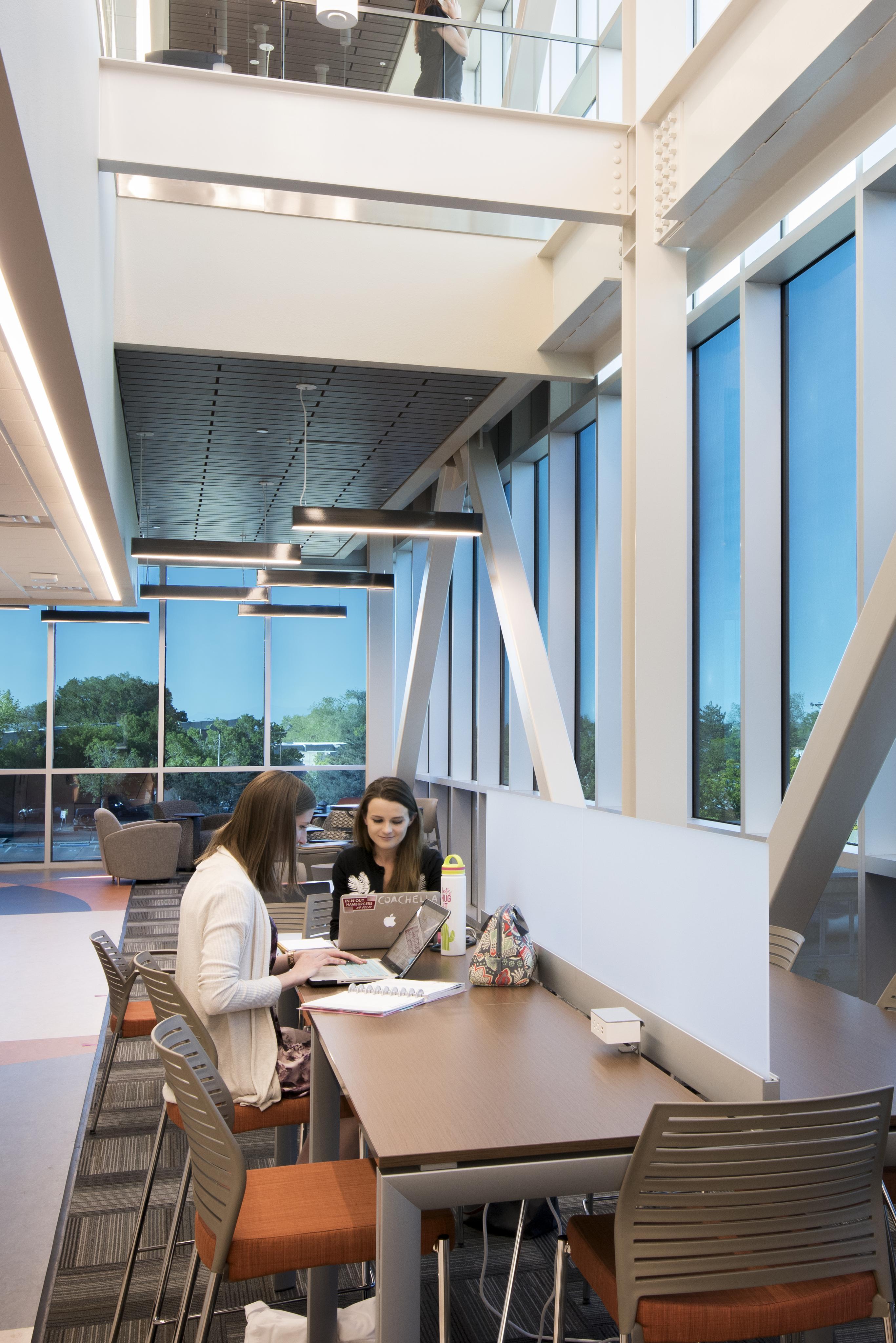 Two coworkers collaborating at a table in the common space of an office building with smart glass windows. 