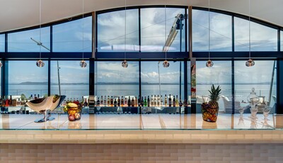 Landscape shot looking at a long hotel bar with glass behind it, where you can see clouds.