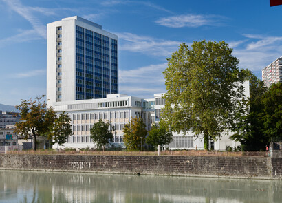 Façade of the PAV Pointe Nord Tower. The sky is blue, the new gray building equipped with SageGlass smart windows is on the left of the image. On the right side, there is a tree.