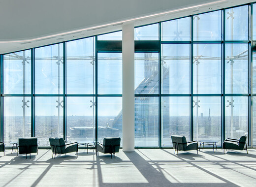 Interior common space of office building with lounge chairs and full smart glass windows from left to right. 