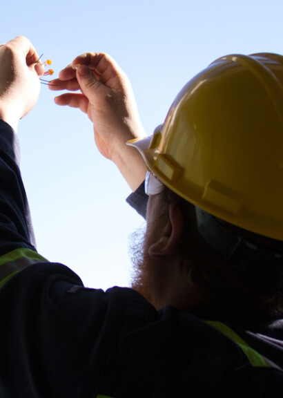 Construction worker holding electrical connection in the air with a shot of the sky in the background. 