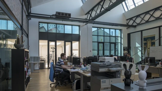 View from the inside of the building. People are working on computers, some windows are tinted, others don't.