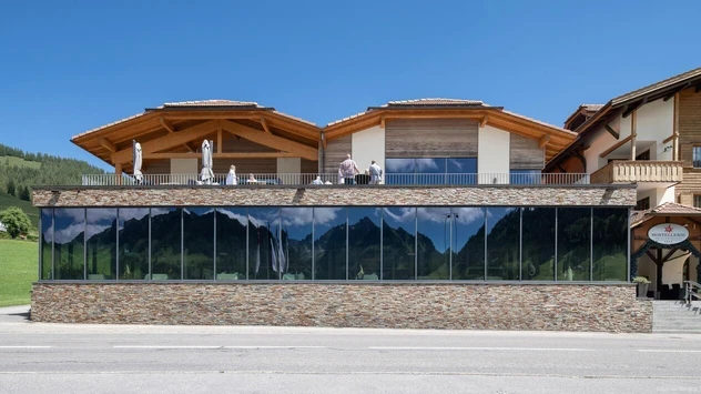 Exterior view of a building with glass and fieldstone on the bottom and a terrace on the top on a sunny day.